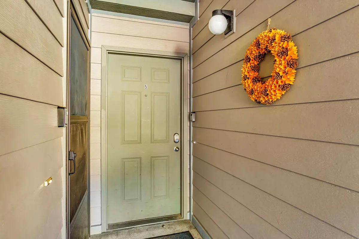 This image focuses on the condo's front door adorned with a decorative wreath and a warm light fixture overhead. The entryway is well-lit and inviting, clearly showing a step-free threshold that allows for effortless access right at arrival.