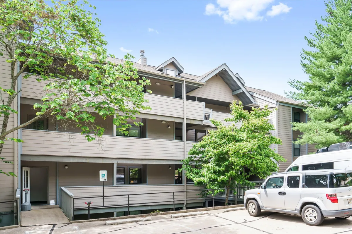 A casual view of the community exterior featuring a leafy tree, balconies with railings, and a well-maintained parking area. The scene conveys a relaxed atmosphere and easy outdoor access right outside the unit.