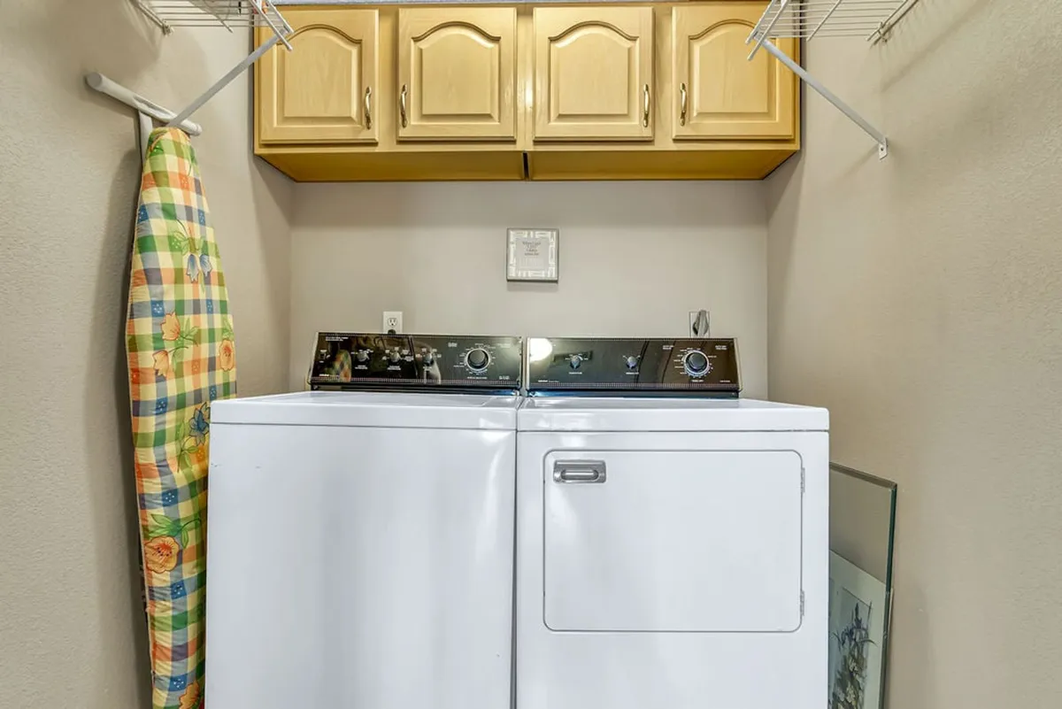 A practical laundry area featuring a washer, dryer, cabinets, and an ironing board. The space appears well-organized and convenient for extended stays.