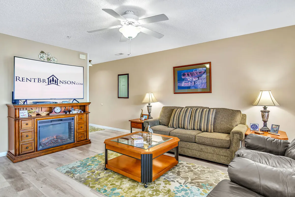 A comfortable living room scene with a sofa, coffee table, TV, lamps, and artwork. The space is arranged for easy socializing, watching movies, or relaxing with family and friends.