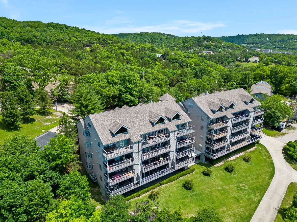 A tranquil exterior view of a three-story building surrounded by lush greenery, with balconies that offer open vistas. The natural landscape and elevated decks set the scene for peaceful relaxation and scenic enjoyment.