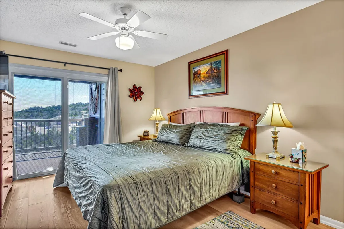 A tranquil bedroom with a plush bed, nightstand, window view, soft lighting, and calming wall art. The layout and decor support a restful ambiance and offer a hint of scenic views from the bedroom window.
