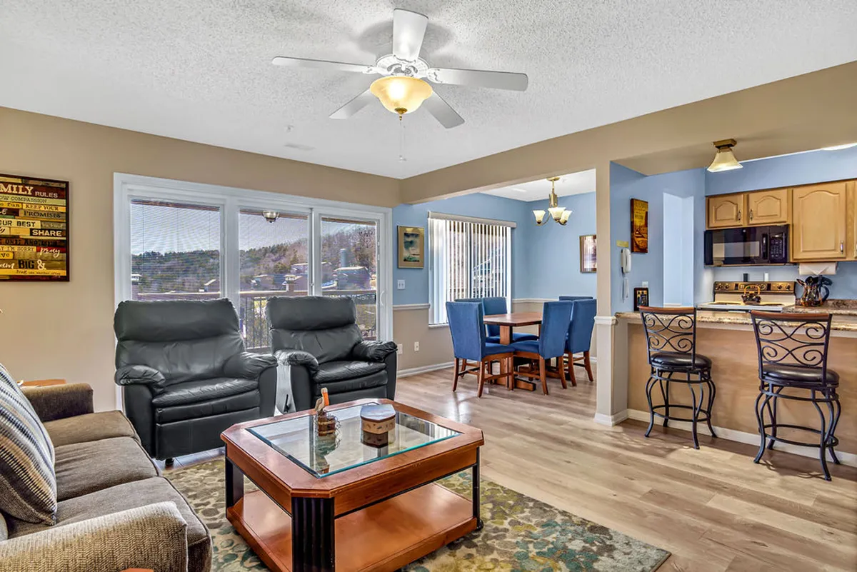 The image showcases a bright, open-concept living space with plush recliners in front of an electric fireplace, a stylish kitchen bar, and a cozy dining area. Sunlight pours in, highlighting the inviting atmosphere perfect for relaxing or gathering with loved ones.