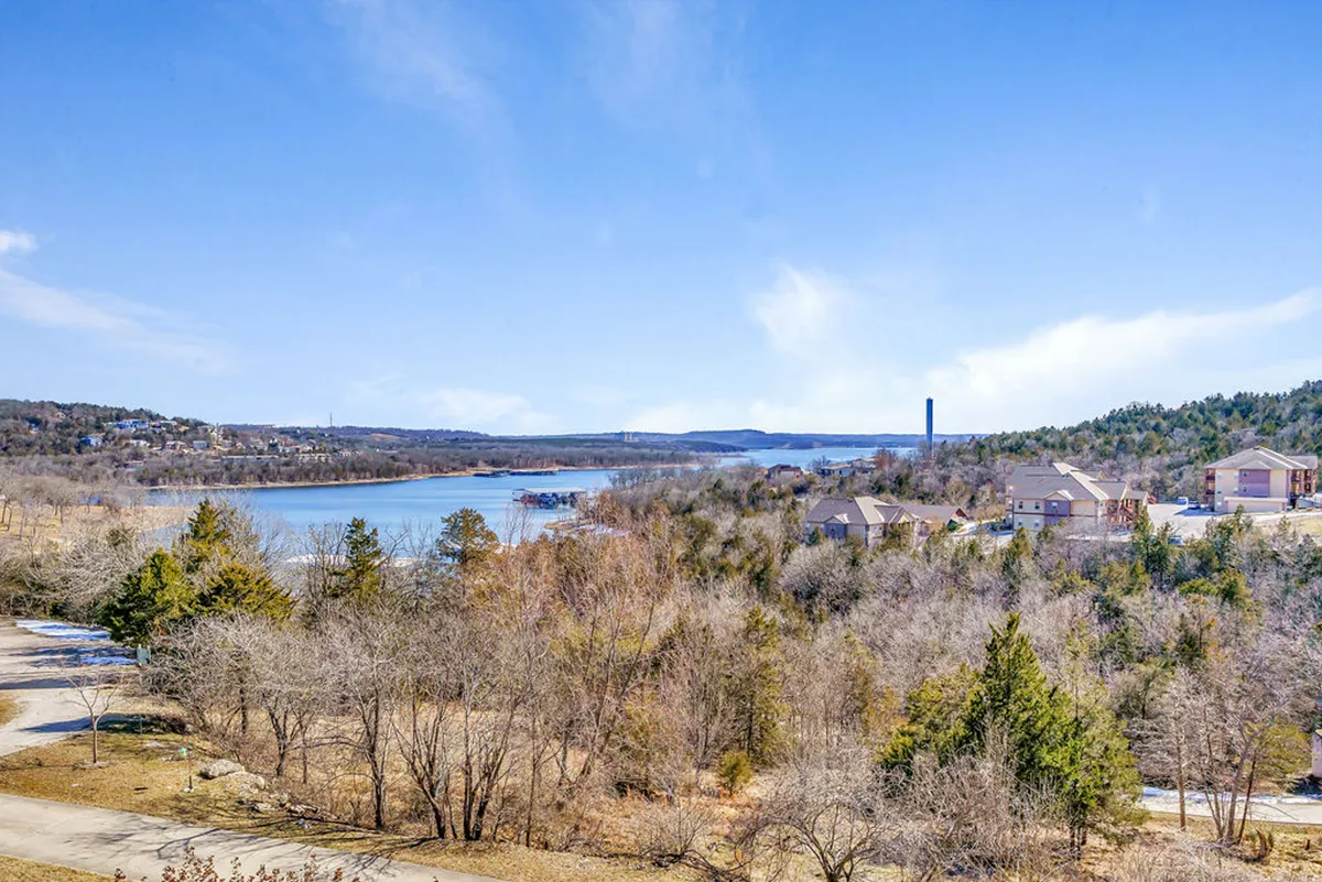 A tranquil view of Table Rock Lake, with calm blue waters stretching toward distant hills and a few residential buildings nestled along the shoreline. The setting sun casts a golden glow over the lake, enhancing its serene beauty and highlighting the recreational opportunities available.