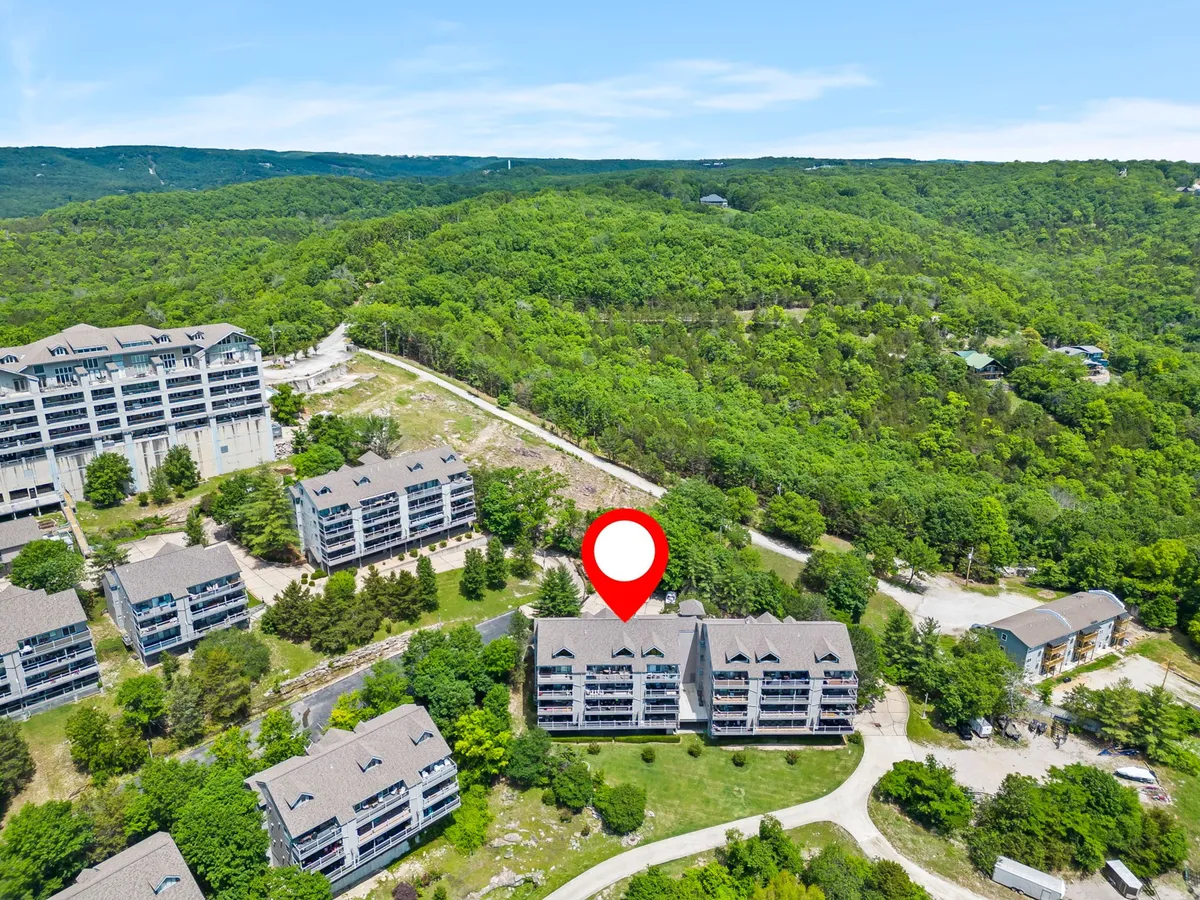 An inviting view of a green hillside dotted with resort buildings and a winding road leading into the property. The designated location marker signals convenience and accessibility, while the expansive landscape connects the resort to the broader Branson area.