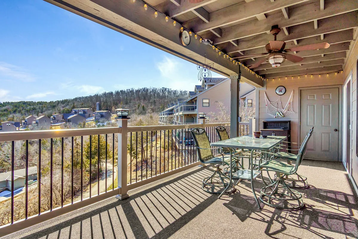 An inviting outdoor dining area with a table and comfortable seating, decorated with string lights and a ceiling fan. The deck overlooks scenic hills, providing a perfect spot for enjoying meals or drinks as the sun sets.