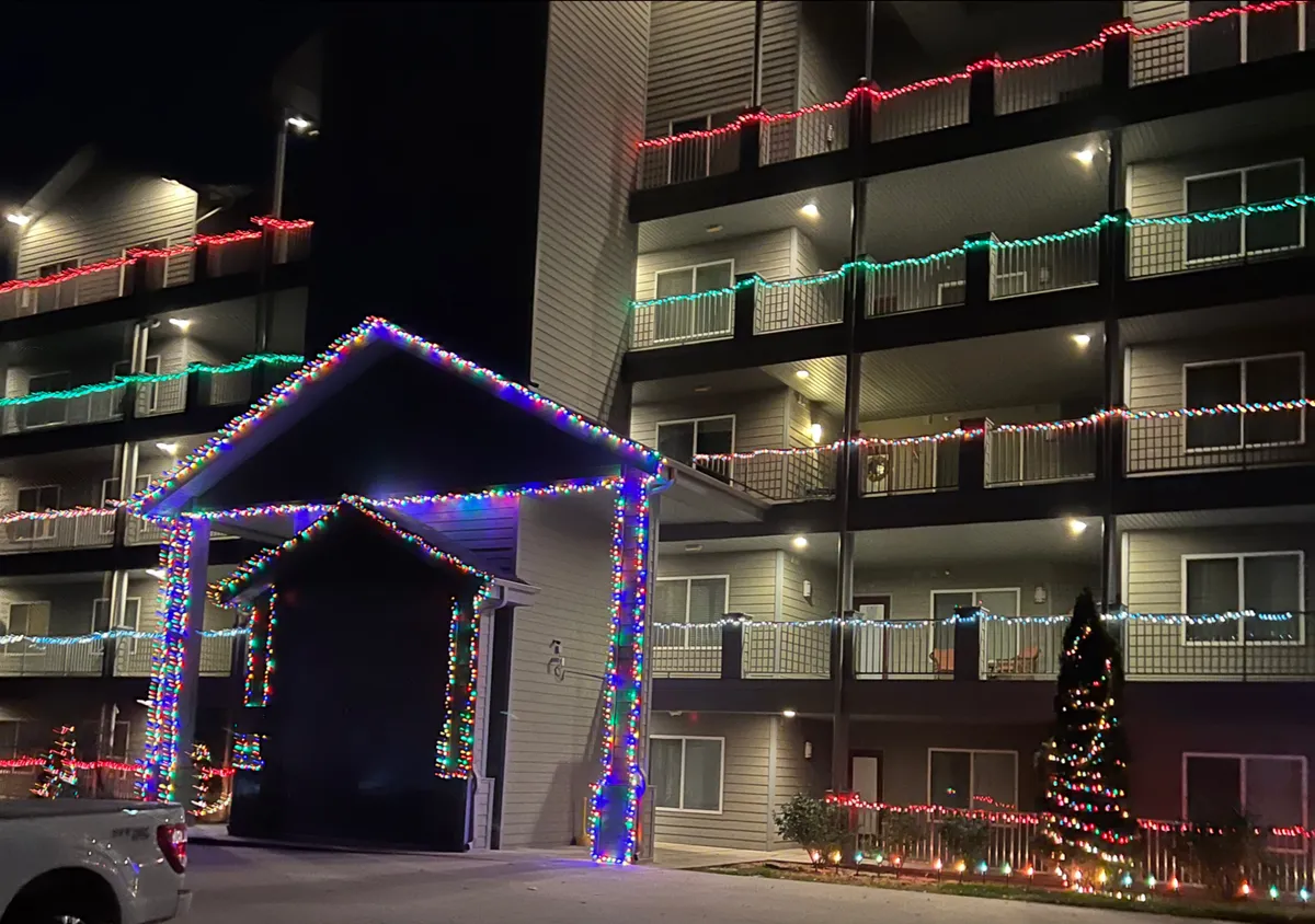 The scene captures a decorated exterior entrance adorned with colorful lights, balconies lit up, and a shining Christmas tree. The joyful mood and communal feel reflect a sense of belonging and celebration, evoking the lively Branson entertainment experience.
