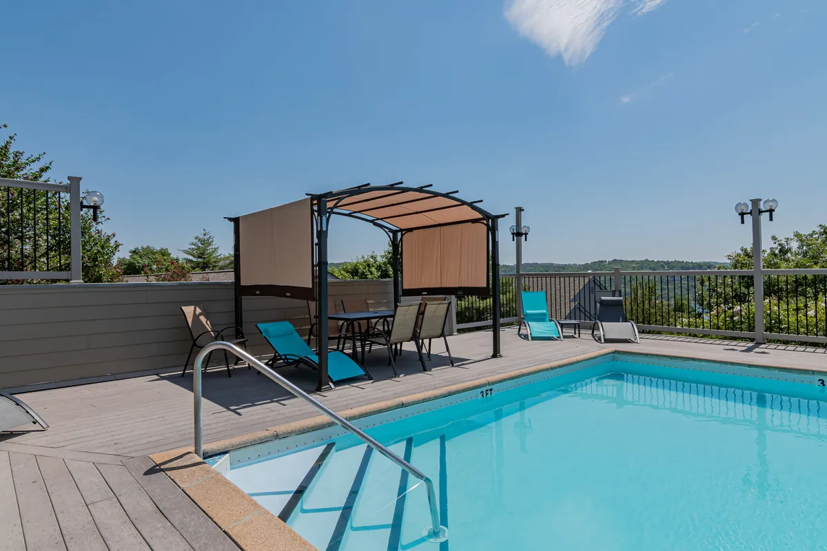 A beautifully landscaped outdoor pool area featuring a swimming pool, a canopy gazebo, and an array of lounge chairs. The setting suggests both leisure and social opportunities, with a scenic landscape view in the background.